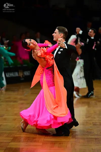 Dancesport competitor: Female dancer: bright pink latin dress with orange/peach-colored flowing fabric 