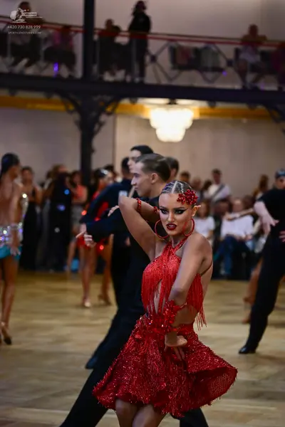 Dancesport competitor: Foreground female dancer: red Latin dress with sequins and fringe, red floral ha