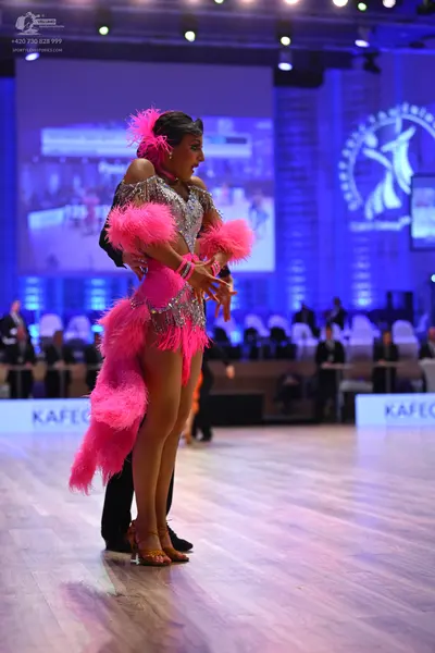 Dancesport competitor: Female dancer: silver sequin Latin dress with bright pink feather trim on the he