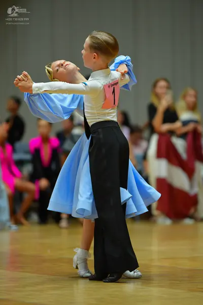 Dancesport competitor: Female dancer: white long-sleeved top with large, flowing light blue sleeves and