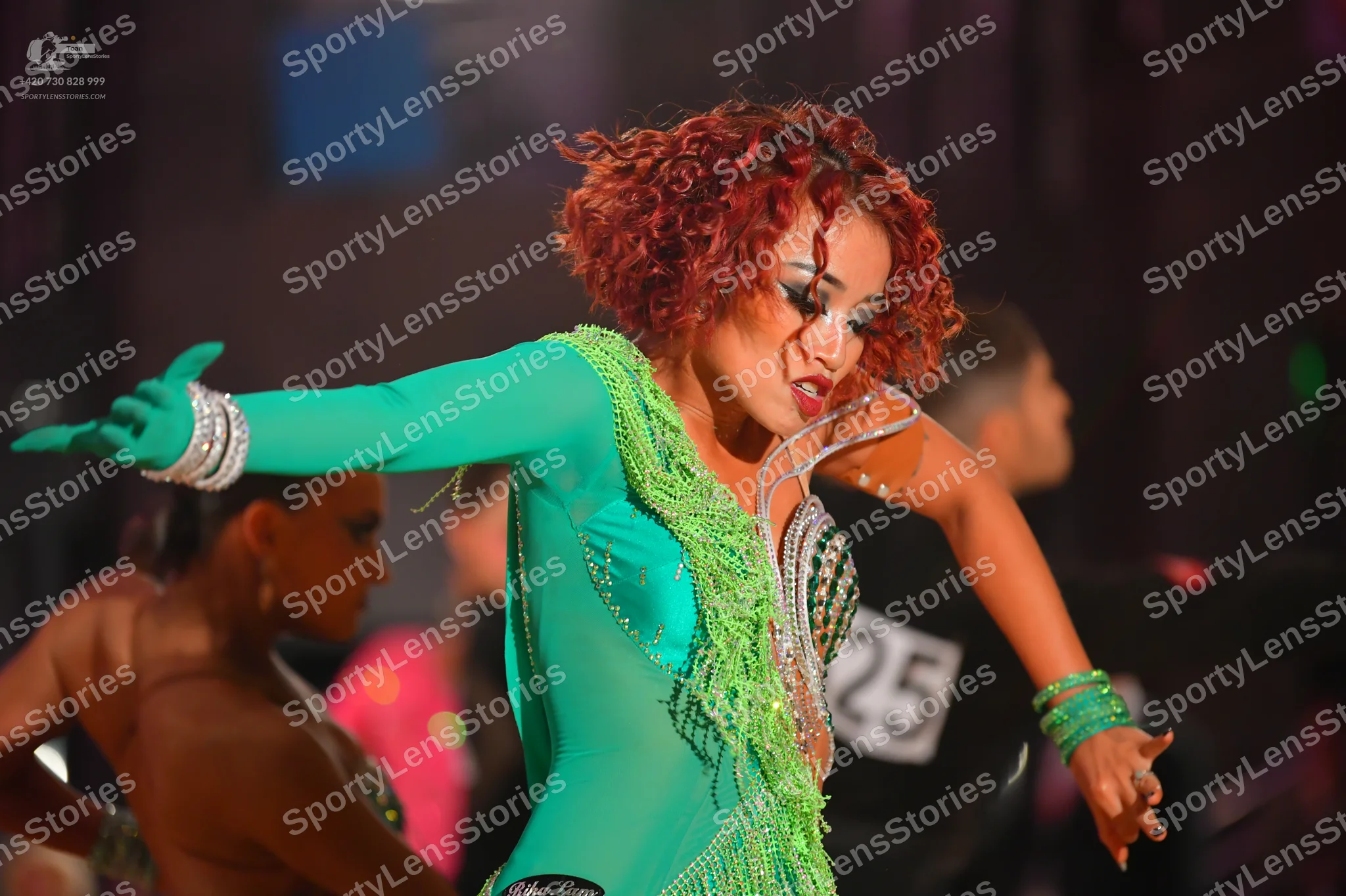 Dancesport competitor #25: Foreground female dancer: green long-sleeved latin dress with sequins, fringe, a