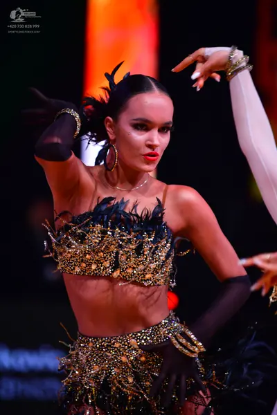 Dancesport competitor: Female dancer: black two-piece Latin dance costume heavily embellished with gold
