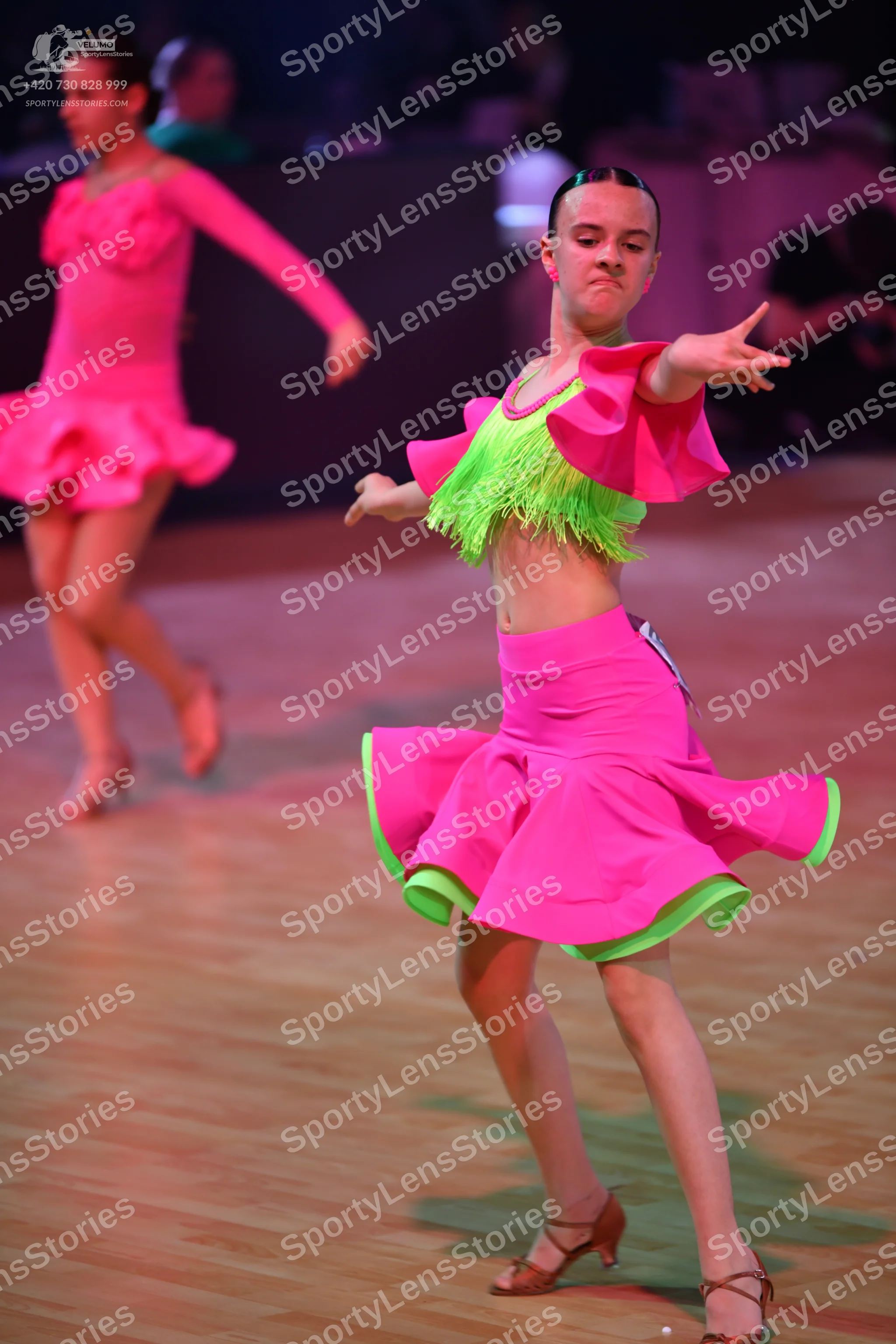 Dancesport competitor: Female dancer in foreground: pink and lime green latin dress featuring a fringed