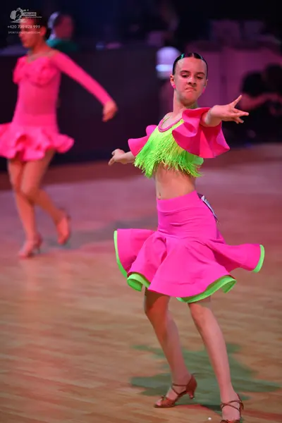 Dancesport competitor: Female dancer in foreground: pink and lime green latin dress featuring a fringed