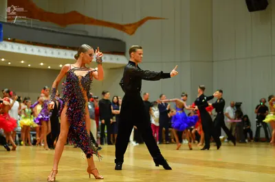 Dancesport competitor: Foreground female dancer: dark Latin dress with multicolored sequins (pink, blue