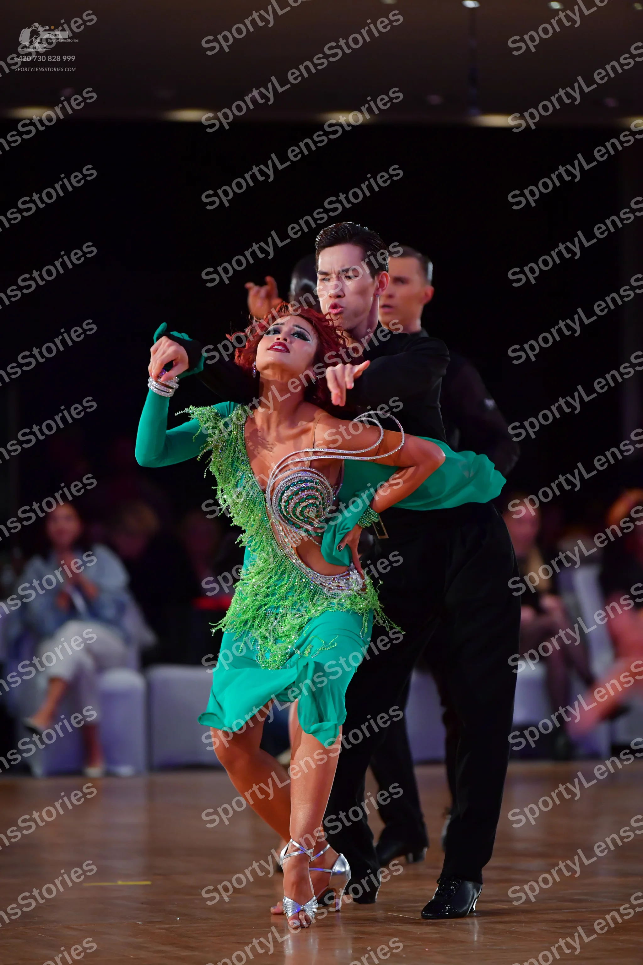 Dancesport competitor: Female dancer: green Latin dress with long sleeves, fringe detailing, and a swir