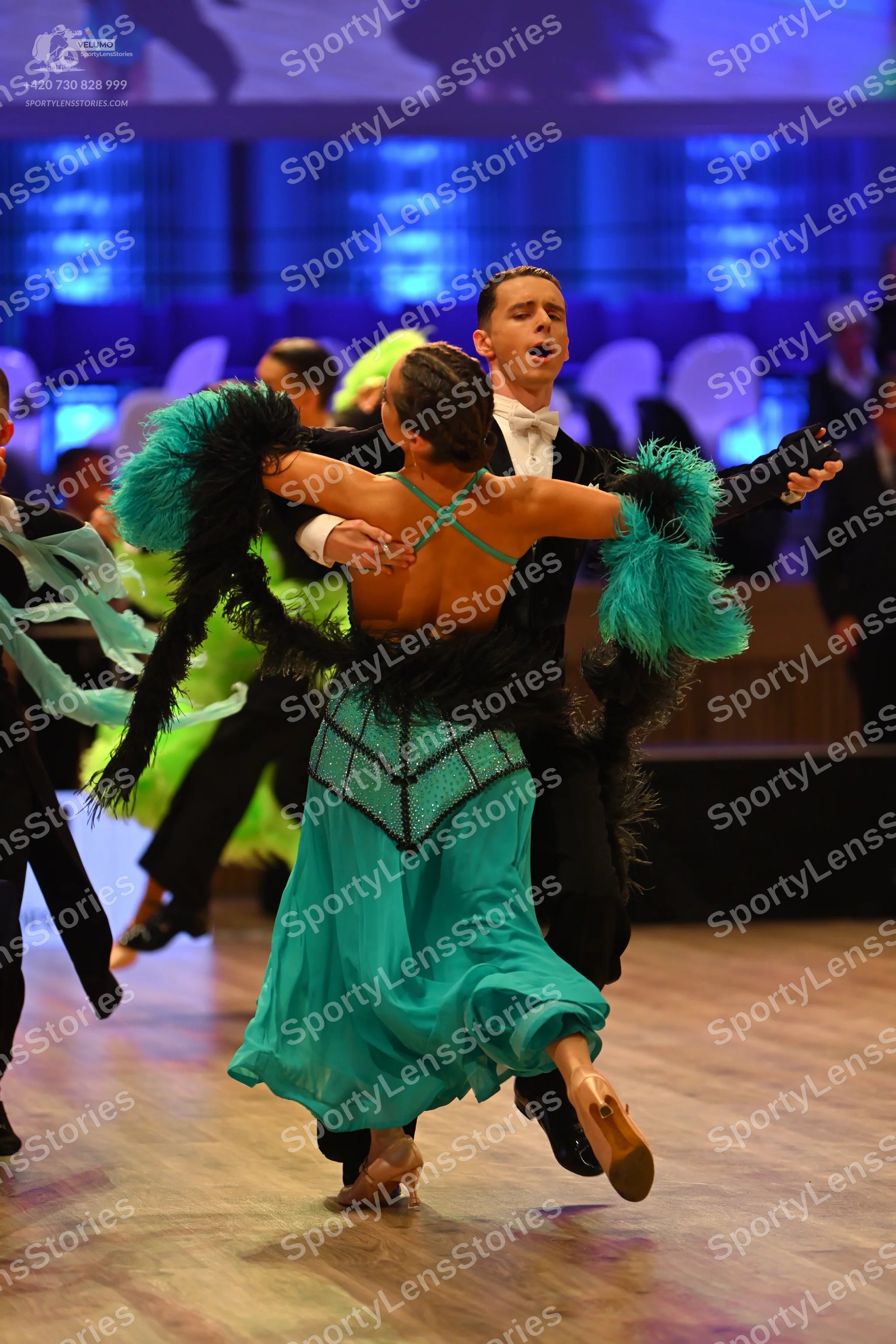 Dancesport competitor: Female dancer: teal and black Latin dance dress with an open back, teal criss-cr