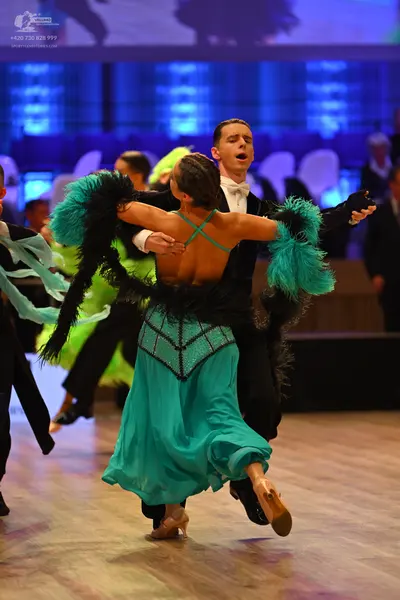 Dancesport competitor: Female dancer: teal and black Latin dance dress with an open back, teal criss-cr