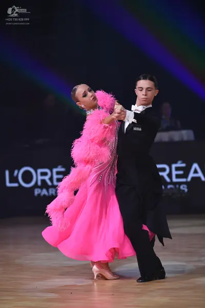 Dancesport competitor: Female dancer: bright pink ballgown with feathery embellishments and a sparkly b
