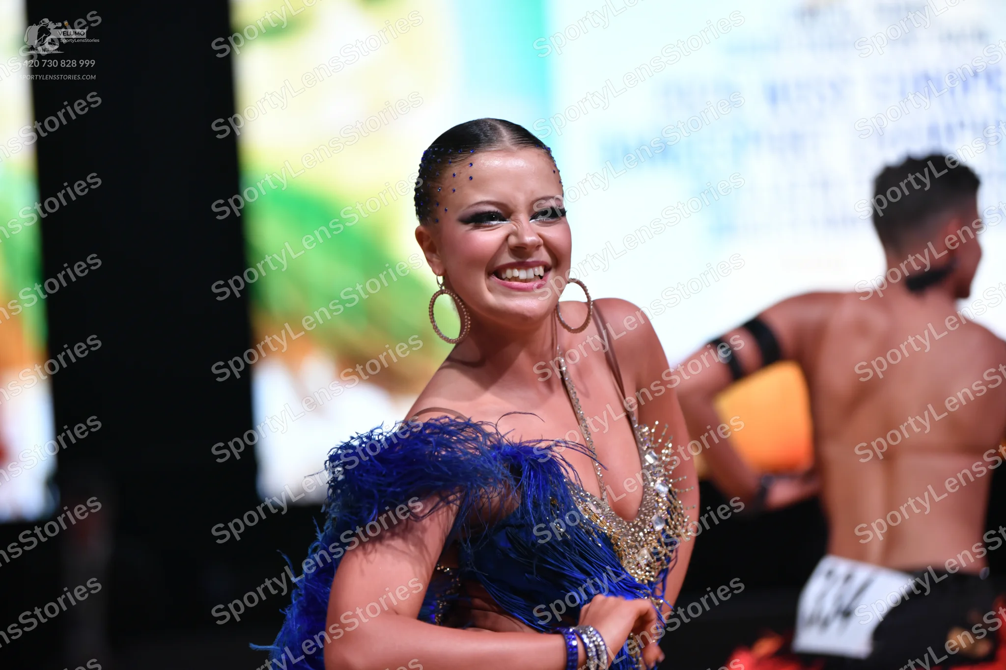 Dancesport competitor: Female dancer: blue Latin dress with blue feather trim and gold/nude sequined bo