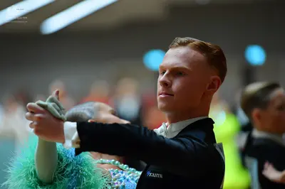 Dancesport competitor: Male dancer: black suit with "PICANTE" text on the sleeve and white shirt cuffs 