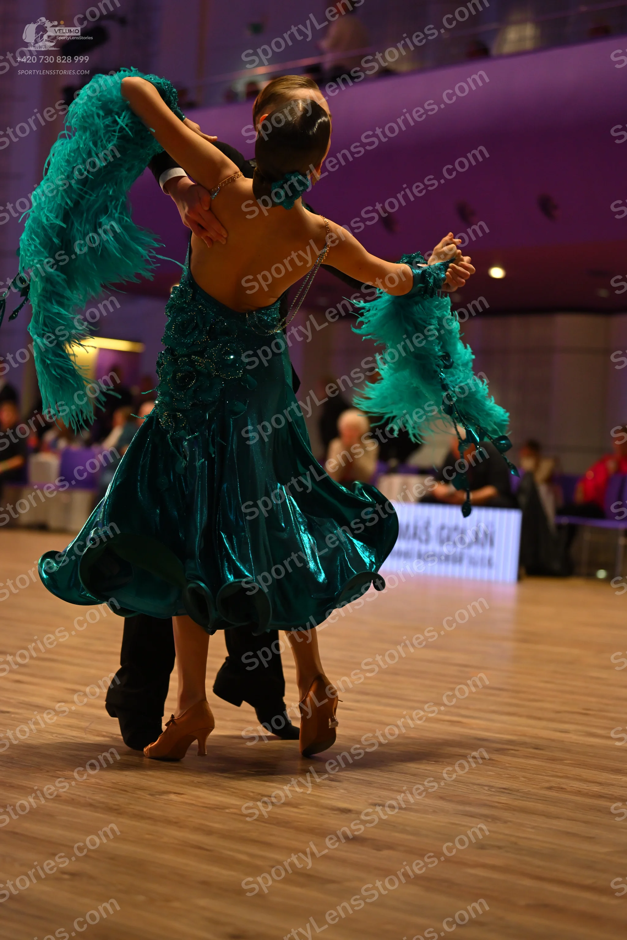 Dancesport competitor: Female dancer: teal latin dress with a shiny fabric and large teal feather-like 