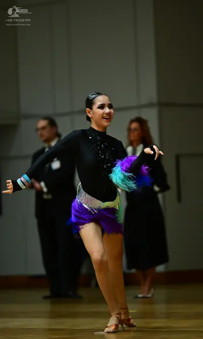 Dancesport competitor: Female dancer (foreground): black long-sleeved Latin dance dress with black sequ