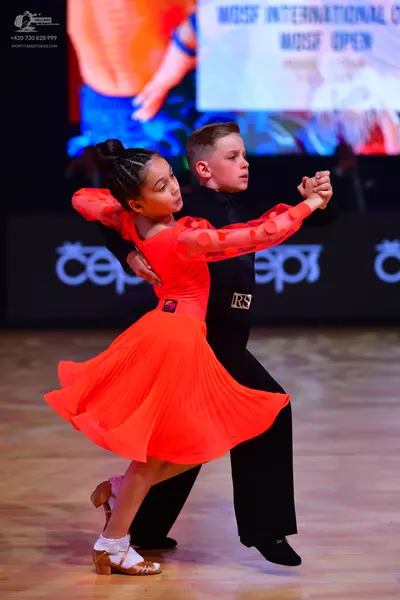 Dancesport competitor: Female dancer: red Latin dress with long, sheer sleeves featuring red circular e