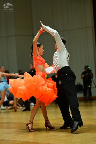 Dancesport competitor: Female dancer: orange Latin dress with a voluminous tulle skirt and orange wrist