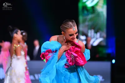 Dancesport competitor: Female dancer in foreground: bright blue voluminous ballroom dress with large pi