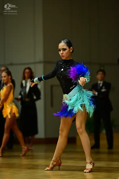 Dancesport competitor: Female dancer in foreground: black long-sleeved latin dress with a vibrant purpl