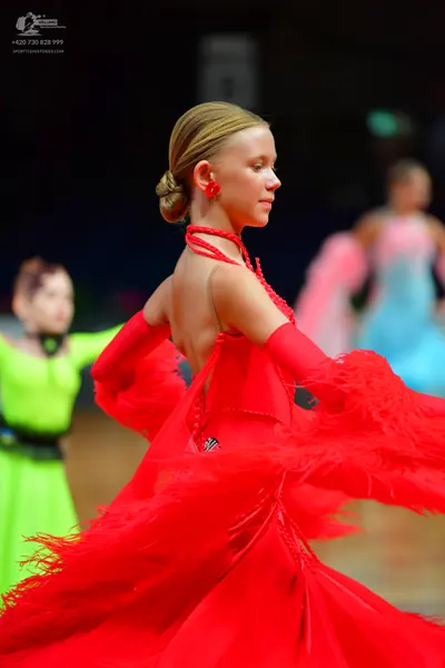 Dancesport competitor: Female dancer in foreground: red latin dress with long sleeves, large ruffled sk