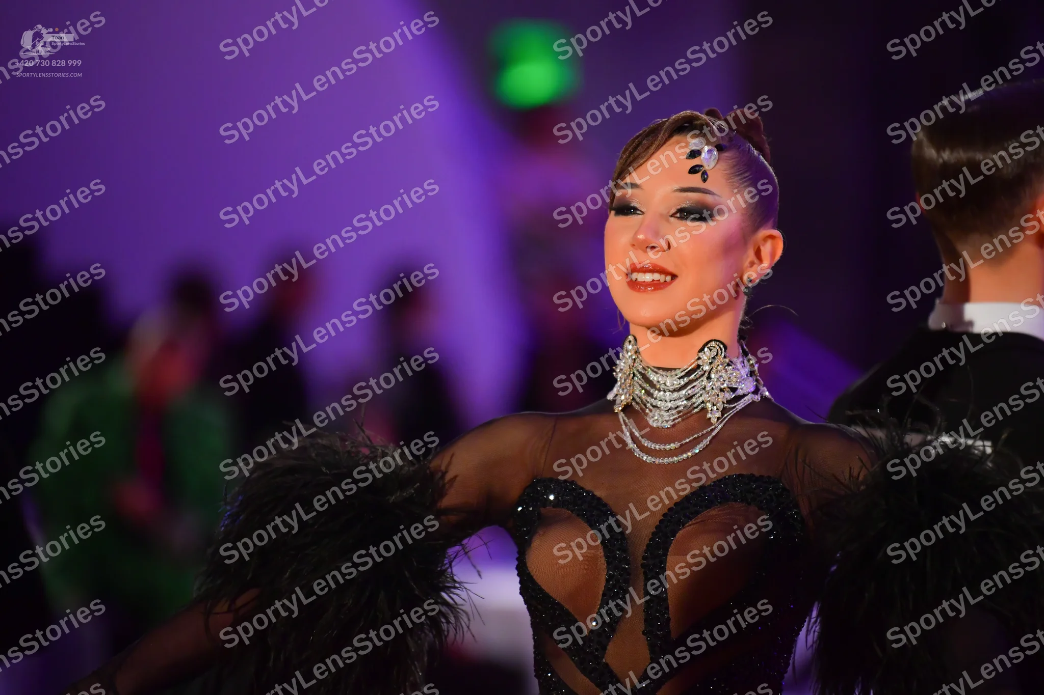 Dancesport competitor: Female dancer: black latin-style bodysuit with sheer mesh panels, large black se