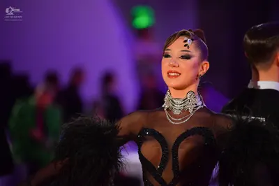 Dancesport competitor: Female dancer: black latin-style bodysuit with sheer mesh panels, large black se
