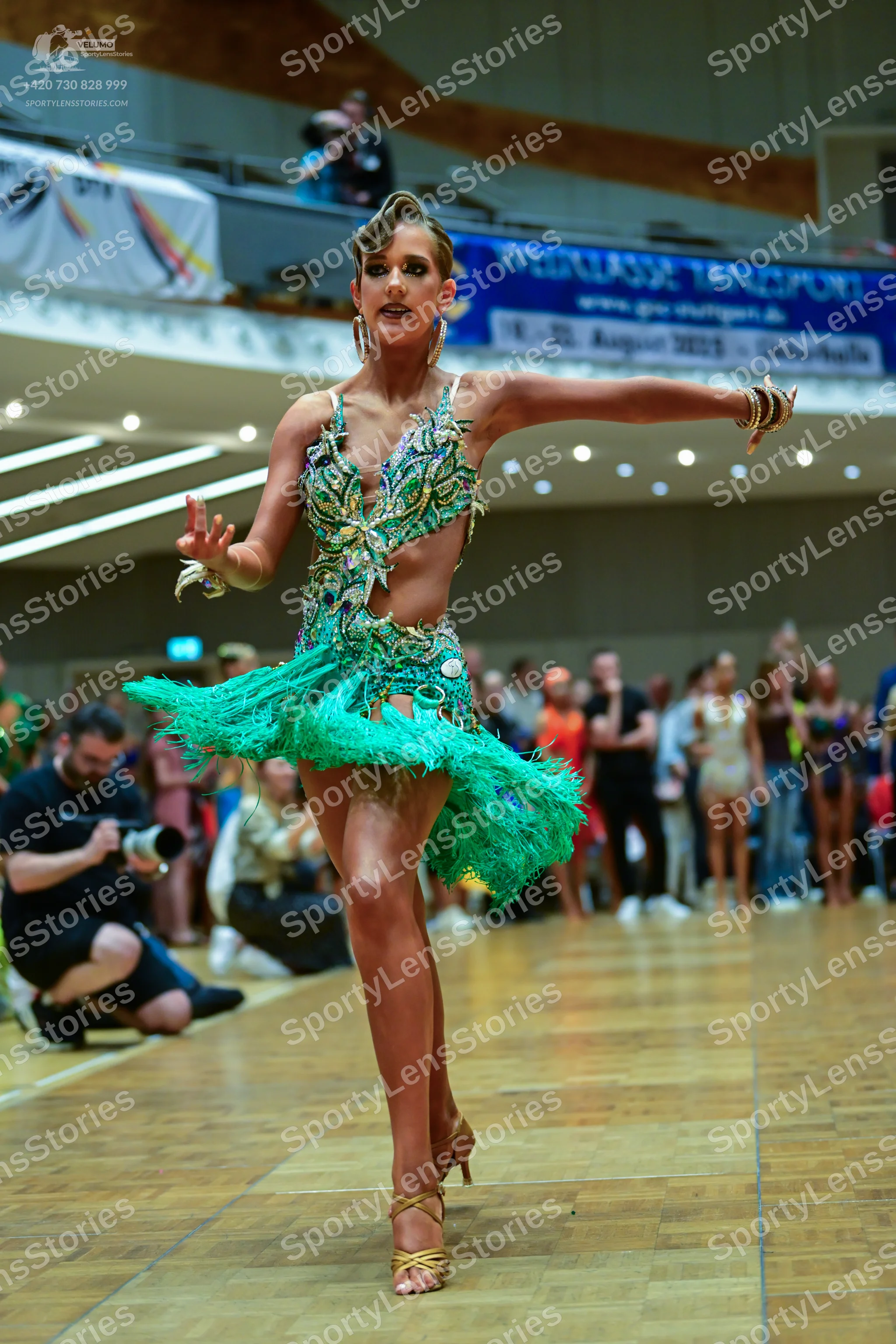 Dancesport competitor: Female dancer: teal and gold Latin dress with a peacock-inspired sequin pattern,