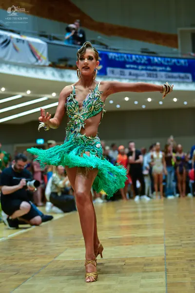Dancesport competitor: Female dancer: teal and gold Latin dress with a peacock-inspired sequin pattern,