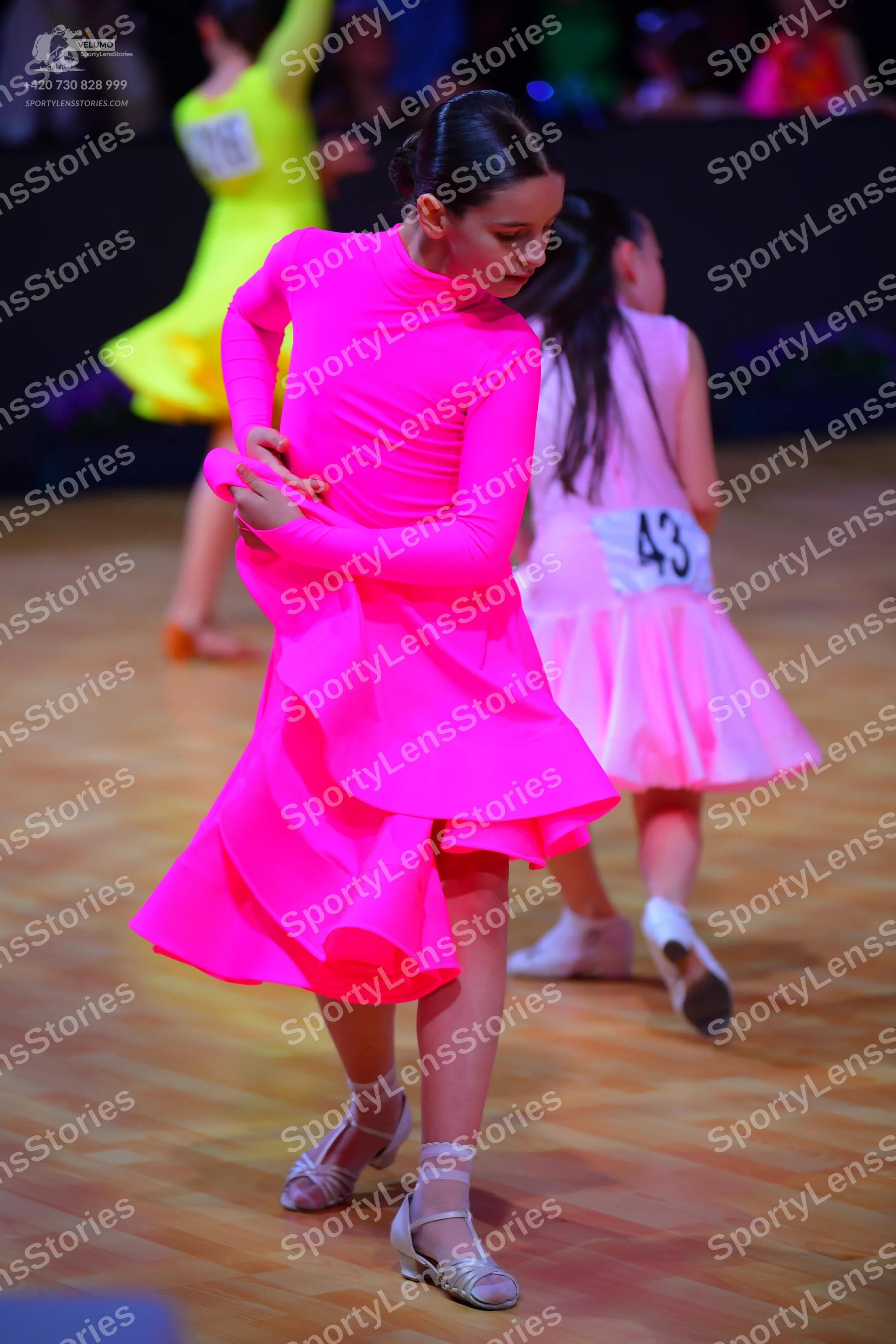 Dancesport competitor: Female dancer in foreground: bright pink, long-sleeved dress with a layered, ruf