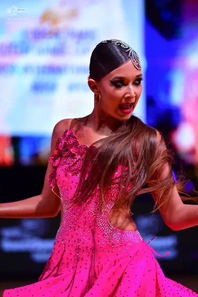 Dancesport competitor: Female dancer: bright pink latin dress with sequins, featuring an asymmetrical s
