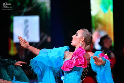 Dancesport competitor: Female dancer: light blue latin dress with large pink ruffled fabric accents, se