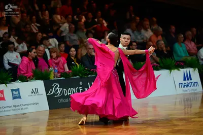 Dancesport competitor: Female dancer: bright pink latin dance dress with long, flowing sleeves