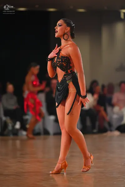 Dancesport competitor: Female dancer in foreground: black latin dress with lace bodice and fringe, wear