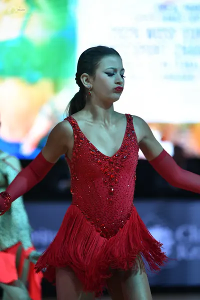 Dancesport competitor: Female dancer: red Latin dress with a sequined bodice and fringe skirt, and long