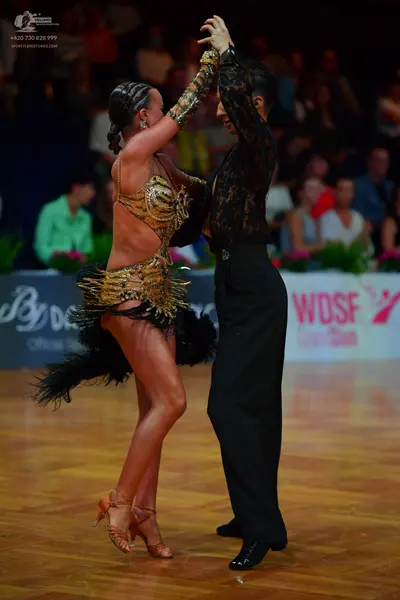Dancesport competitor: Female dancer: gold and black sequined latin dress with black feather trim