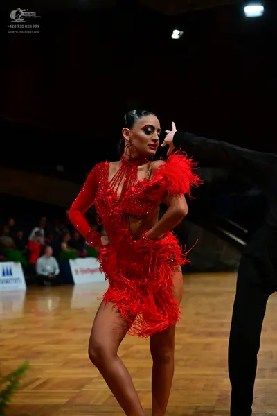 Dancesport competitor: Female dancer: red Latin dress with long sleeves, fringe, and cutouts