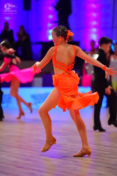 Dancesport competitor: Female dancer in foreground: orange Latin dress with an open back, criss-cross s