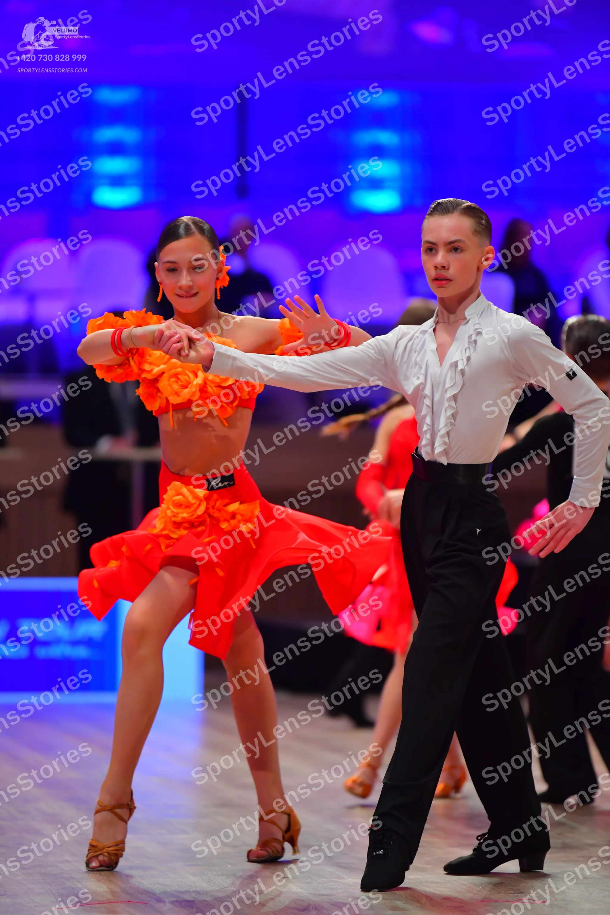 Dancesport competitor: Female dancer: orange and red Latin dance dress with large ruffles and fabric fl