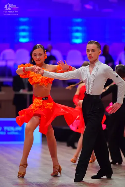 Dancesport competitor: Female dancer: orange and red Latin dance dress with large ruffles and fabric fl