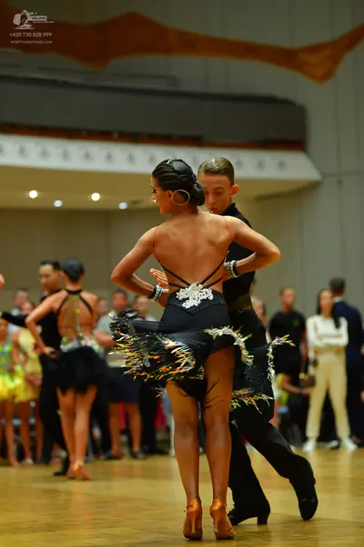 Dancesport competitor: Main female dancer: black latin dress with a backless design, thin straps, white
