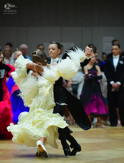 Dancesport competitor: Female dancer: voluminous light yellow ballgown with ruffles, feathers, and sequ