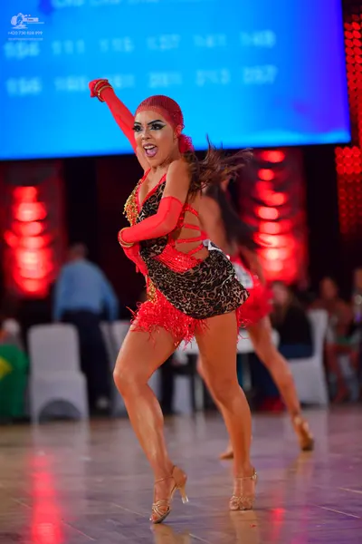 Dancesport competitor: Female dancer in foreground: leopard print Latin dress with red fringe, long red