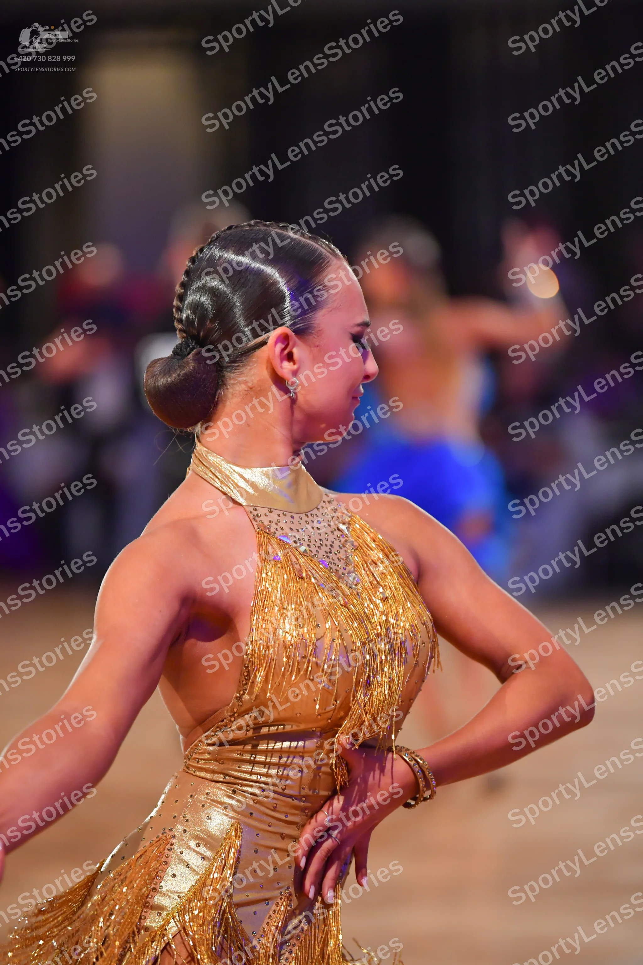 Dancesport competitor: Female dancer in foreground: gold latin dress with sequins and fringe, featuring