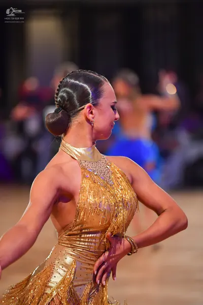 Dancesport competitor: Female dancer in foreground: gold latin dress with sequins and fringe, featuring