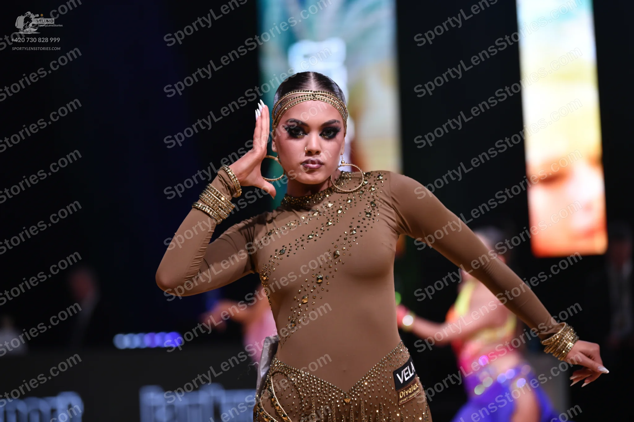 Dancesport competitor: Female dancer in foreground: nude-colored long-sleeved Latin dance costume with 