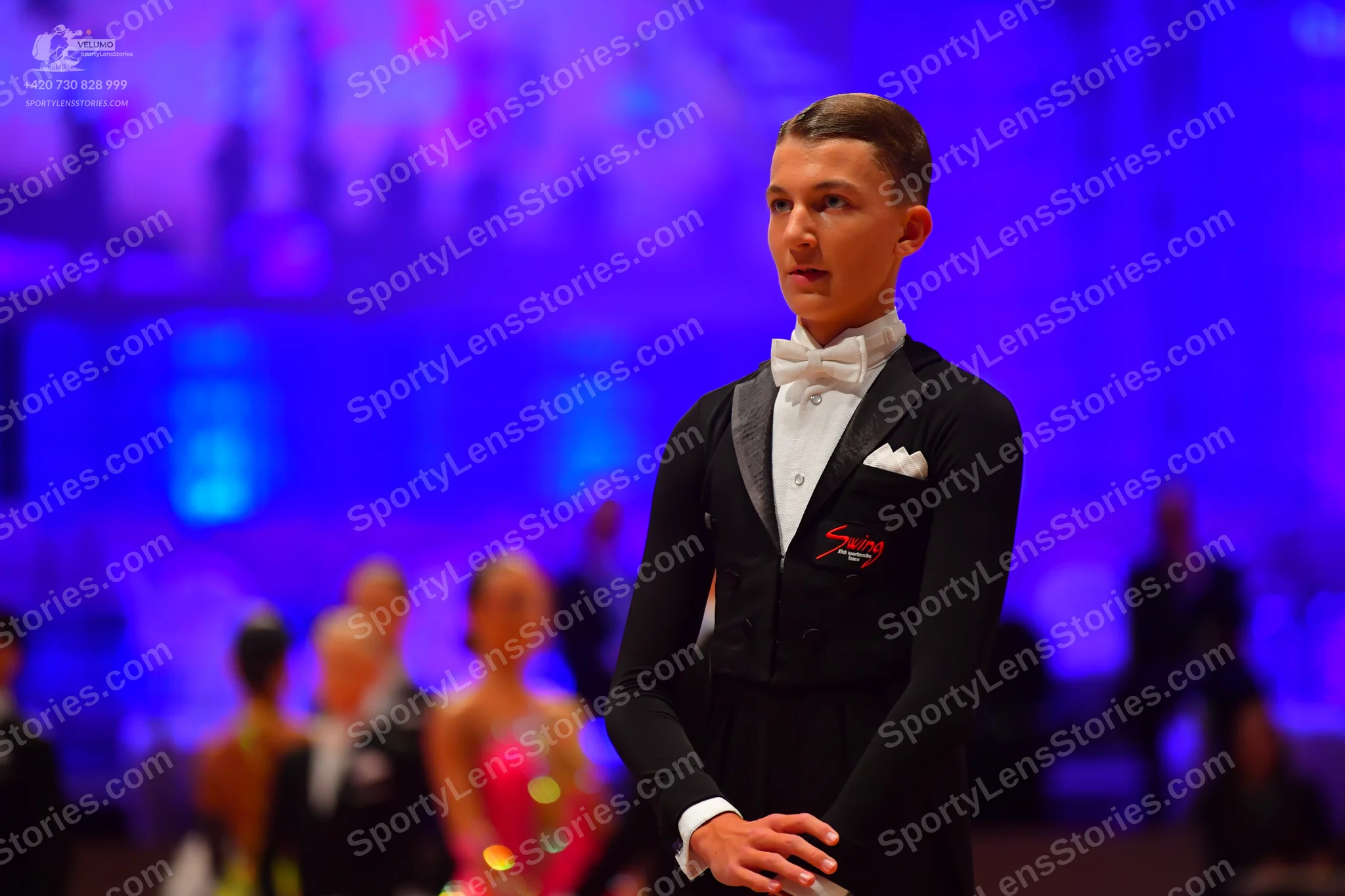 Dancesport competitor: Male dancer: black tuxedo with a white shirt, white bow tie, and white pocket sq
