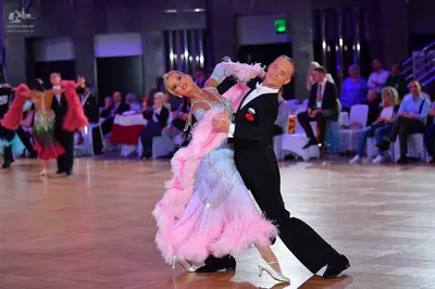 Dancesport competitor: Foreground female dancer: light blue Latin dress with large pink feather trim an