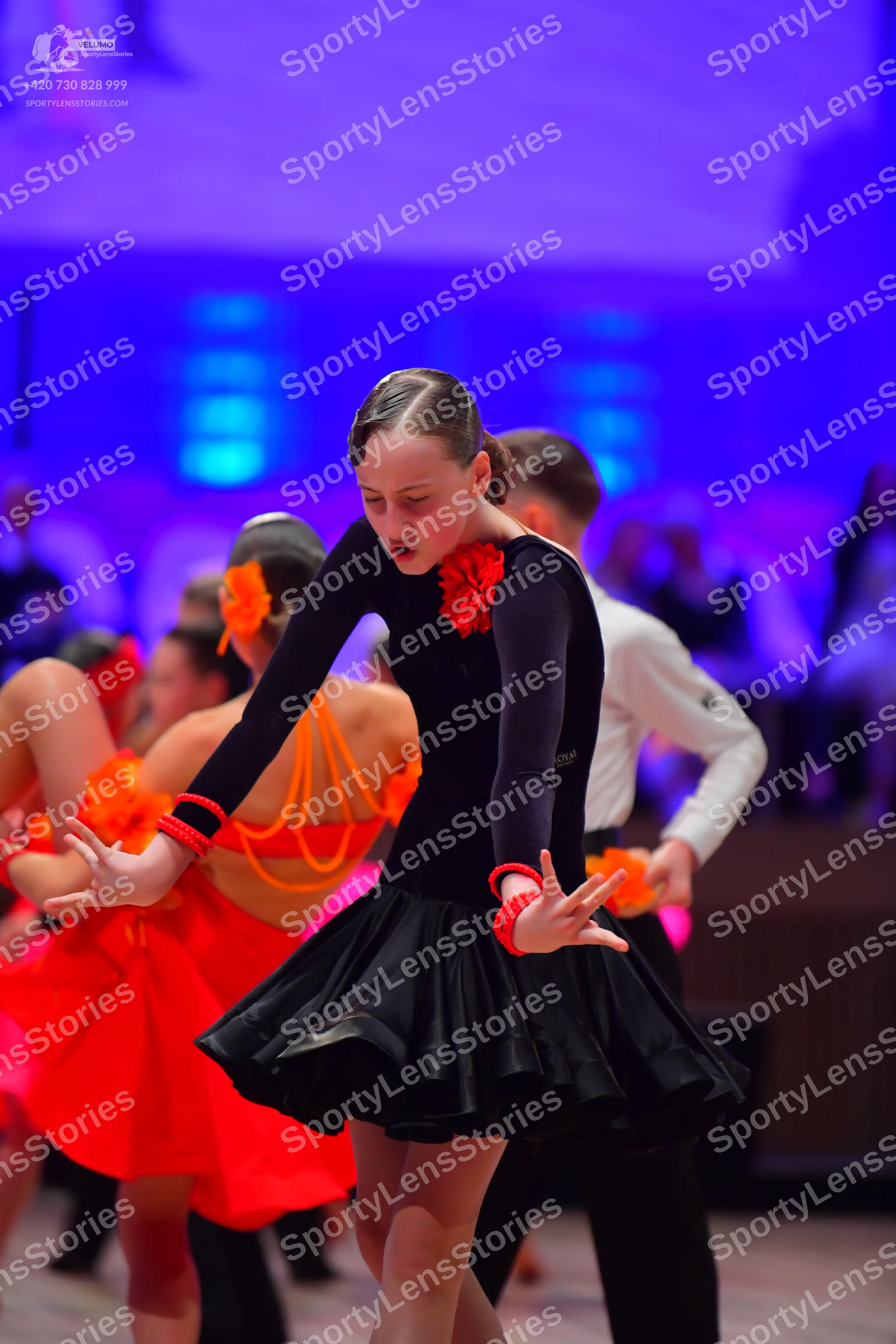 Dancesport competitor: Main female dancer: black long-sleeved Latin dress with a red flower detail at t