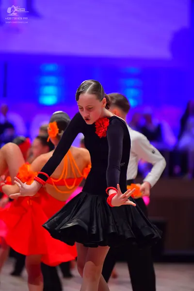 Dancesport competitor: Main female dancer: black long-sleeved Latin dress with a red flower detail at t