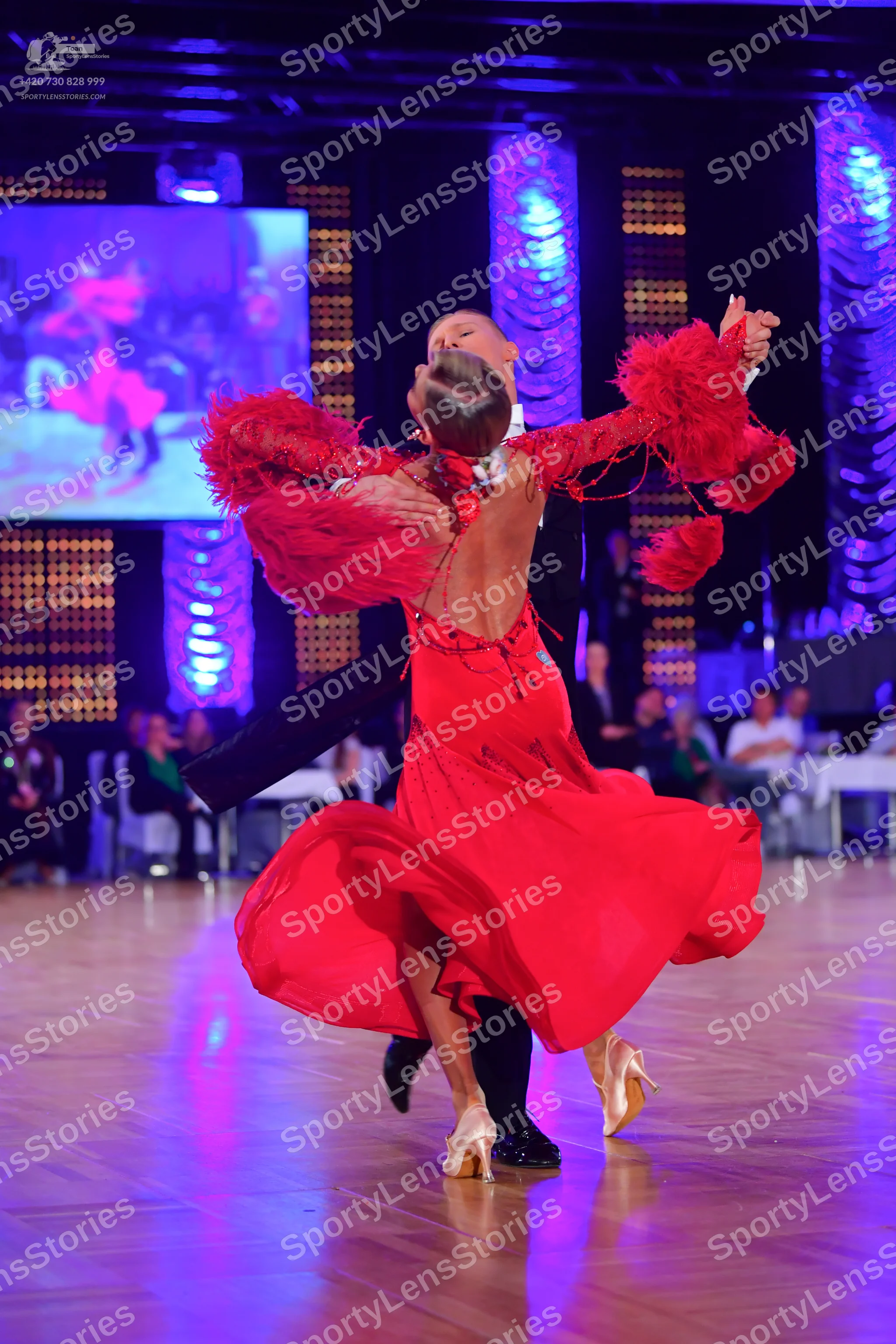 Dancesport competitor: Female dancer: red Latin dress with long, feathered sleeves and a flowing skirt