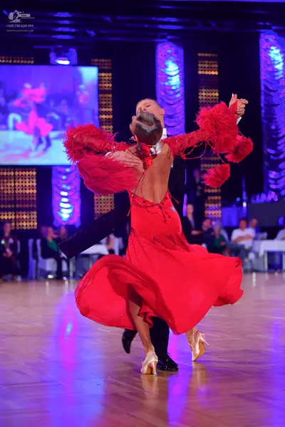 Dancesport competitor: Female dancer: red Latin dress with long, feathered sleeves and a flowing skirt