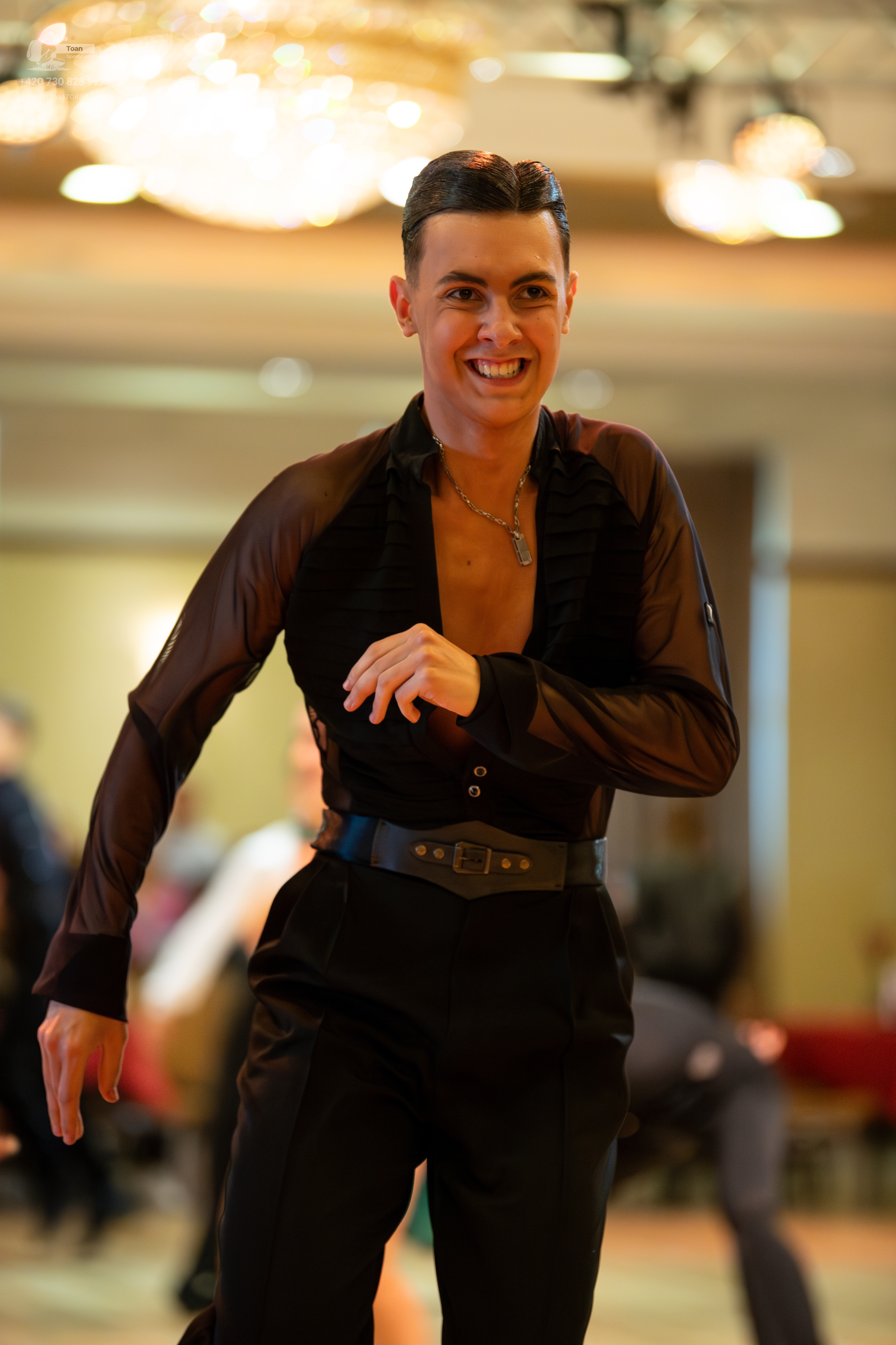 Dancesport competitor: Male dancer: black long-sleeved latin shirt with sheer sleeves, black trousers, 